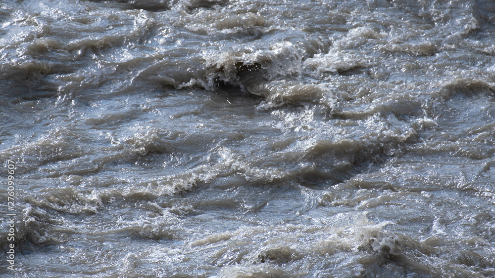 Dirty water in a stormy river. The texture of the water. No people. The rapid flow of the mountain river.