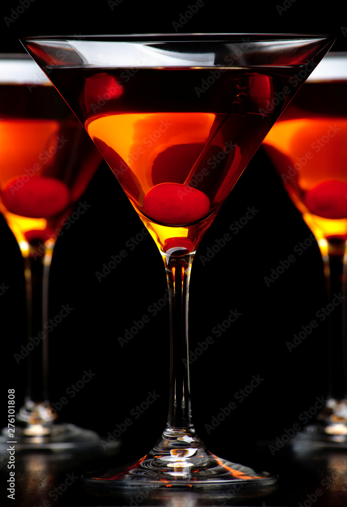 Group of three manhattan drinks in bar with cherry on black