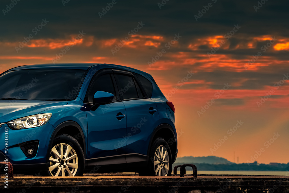 Blue compact SUV car with sport and modern design parked on concrete road by beach at sunset. Hybrid and electric car technology. Car parking space. Automotive industry. Car care business background.