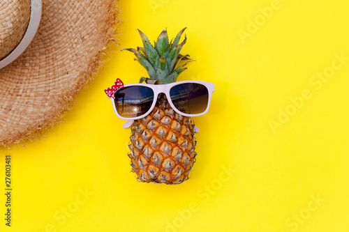 Summer scene. Pineapple in sunglasses and straw hat on yellow background. Concept of holiday on beach, travel, minimalist bright colors, summertime. Colorful female fashion outfit flat lay. Copy space