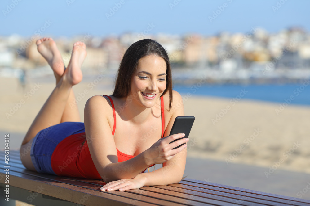 Happy teen in red using smart phone on the beach