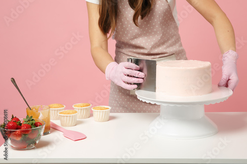 Fotografia, Obraz Close up cropped chef cook confectioner or baker in white t-shirt cooking at table isolated on pink pastel background in studio