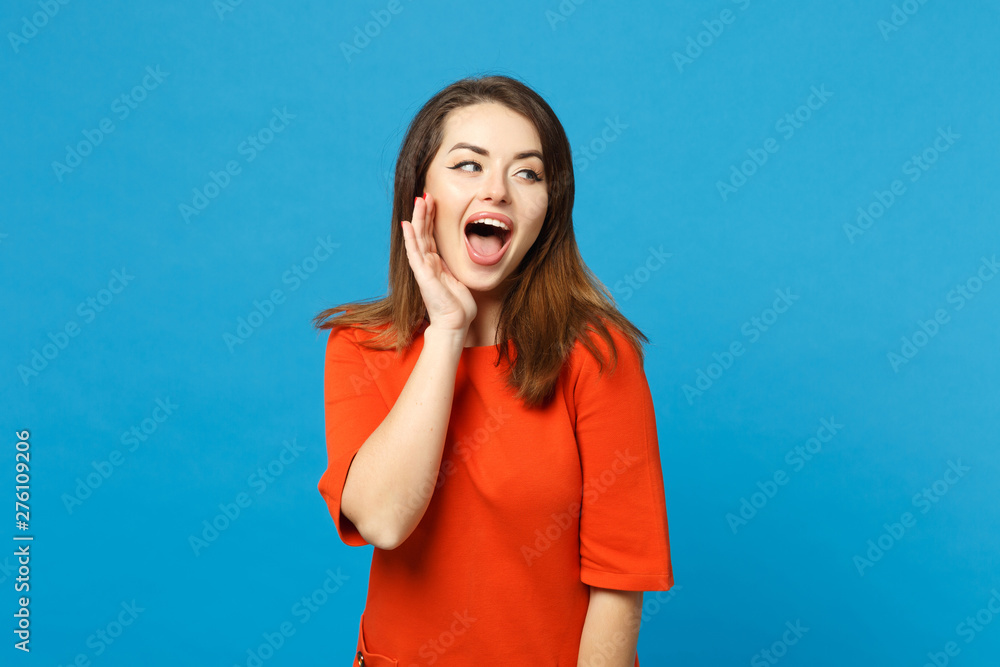 Beautiful brunette young woman wearing red orange dress screaming secret behind her hand isolated over trendy blue background, studio portrait. People lifestyle fashion concept. Mock up copy space. Beautiful brunette young woman wearing red orange dress screaming secret behind her hand isolated over trendy blue background, studio portrait. People lifestyle fashion concept. Mock up copy space.
