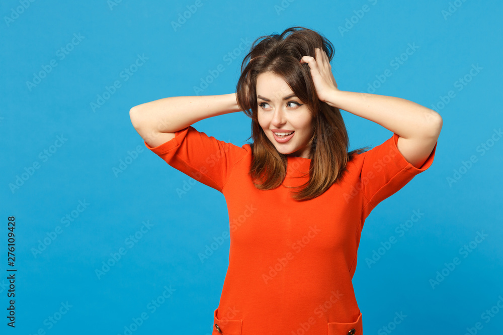 Beautiful brunette young woman wearing red orange dress put hands on head standing posing isolated over trendy blue background, studio portrait. People lifestyle fashion concept. Mock up copy space. Beautiful brunette young woman wearing red orange dress put hands on head standing posing isolated over trendy blue background, studio portrait. People lifestyle fashion concept. Mock up copy space.