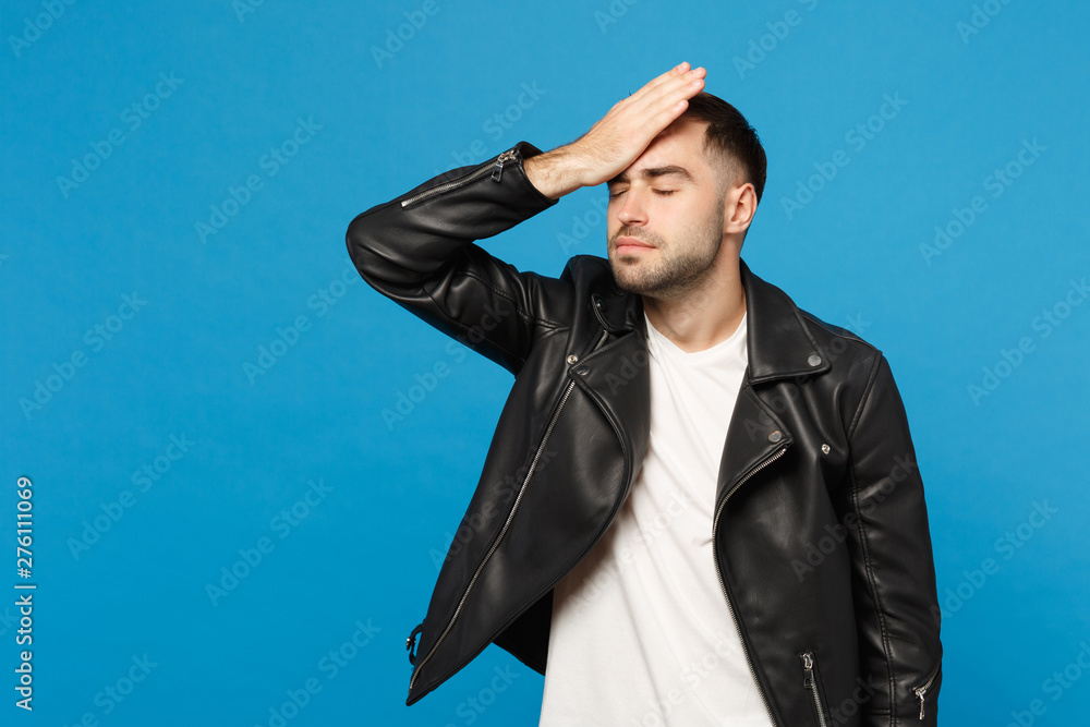 Young sad frustrated worried unshaven man in black jacket white t-shirt put arm on head isolated on blue wall background studio portrait. People sincere emotions lifestyle concept. Mock up copy space. Young sad frustrated worried unshaven man in black jacket white t-shirt put arm on head isolated on blue wall background studio portrait. People sincere emotions lifestyle concept. Mock up copy space.