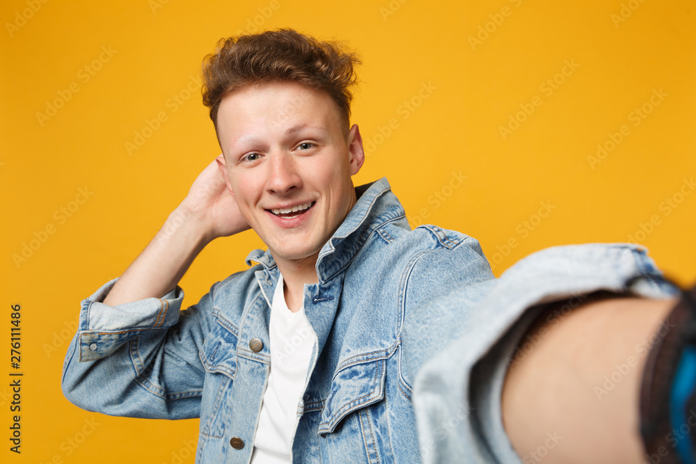 Close up selfie shot of smiling young man in denim casual clothes putting hand on head isolated on yellow orange background in studio. People sincere emotions, lifestyle concept. Mock up copy space. Close up selfie shot of smiling young man in denim casual clothes putting hand on head isolated on yellow orange background in studio. People sincere emotions, lifestyle concept. Mock up copy space.