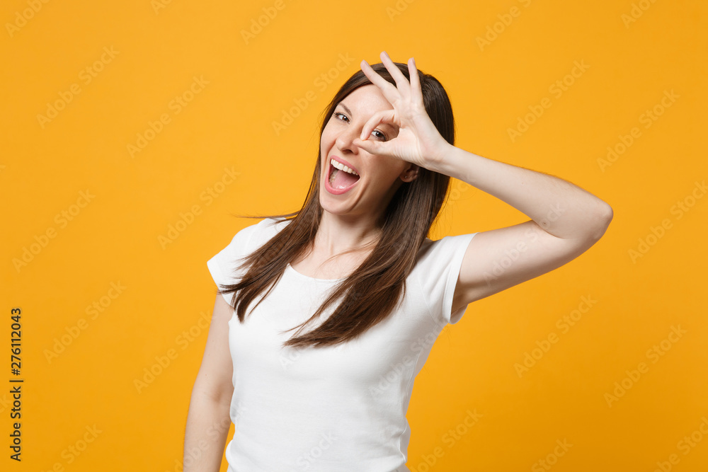 Funny young woman in white casual clothes holding hands near eyes, imitating glasses or binoculars isolated on bright yellow orange background in studio. People lifestyle concept. Mock up copy space. Funny young woman in white casual clothes holding hands near eyes, imitating glasses or binoculars isolated on bright yellow orange background in studio. People lifestyle concept. Mock up copy space.