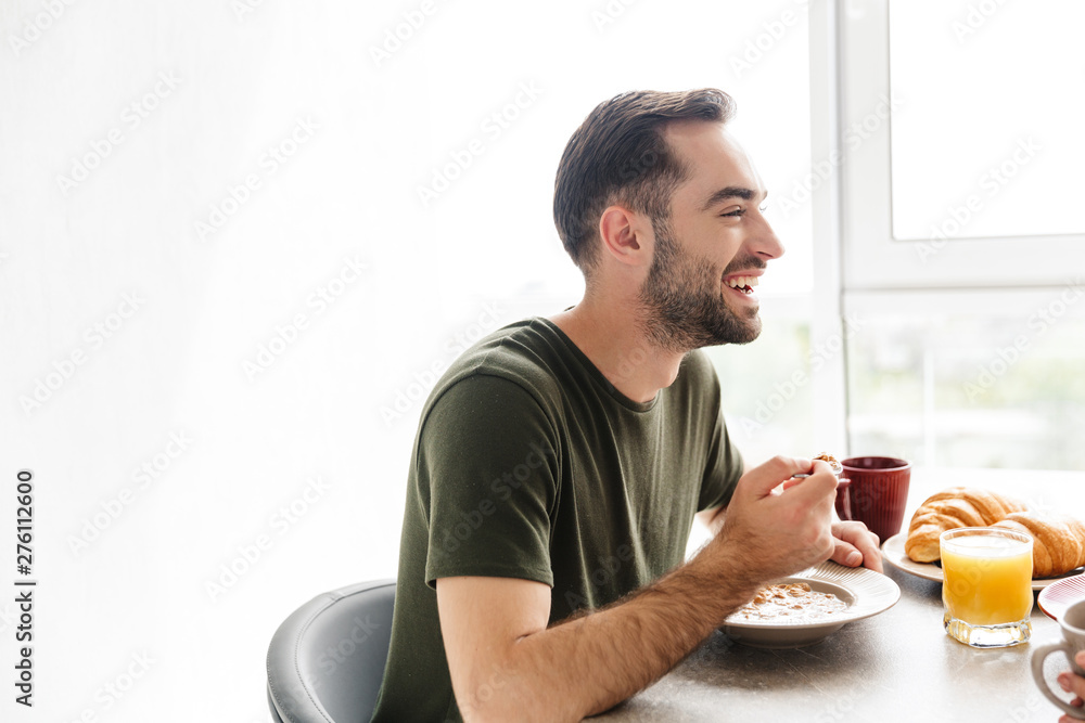 Happy young man indoors at the kitchen have a breakfast eat croissant and corn flakes with milk. Happy young man indoors at the kitchen have a breakfast eat croissant and corn flakes with milk.