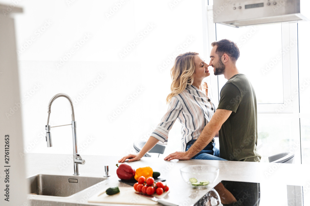 Romantic young loving couple indoors at the kitchen cooking vegetable salad have a breakfast hugging kissing. Romantic young loving couple indoors at the kitchen cooking vegetable salad have a breakfast hugging kissing.