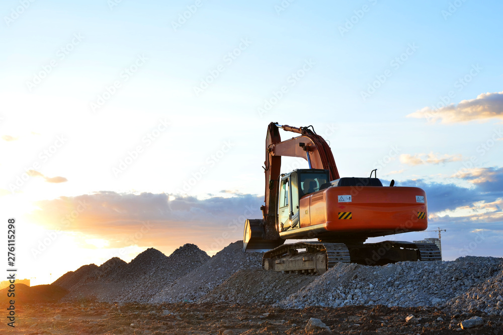 Large tracked excavator works in a gravel pit. Loading of stone and rubble for its processing at a concrete factory into cement for construction work. Cement production factory on mining quarry Large tracked excavator works in a gravel pit. Loading of stone and rubble for its processing at a concrete factory into cement for construction work. Cement production factory on mining quarry