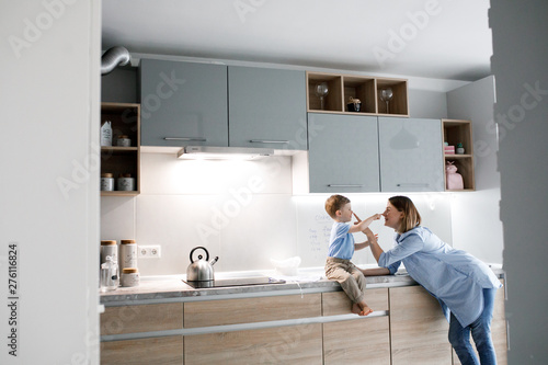 mama and son bake a cookies in kitchen. little boy  wearing a kitchen cloth and head making cookies with his mama