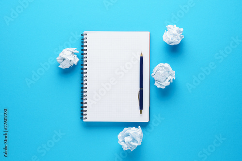 Open notebook, pen and crumpled paper balls on blue background.