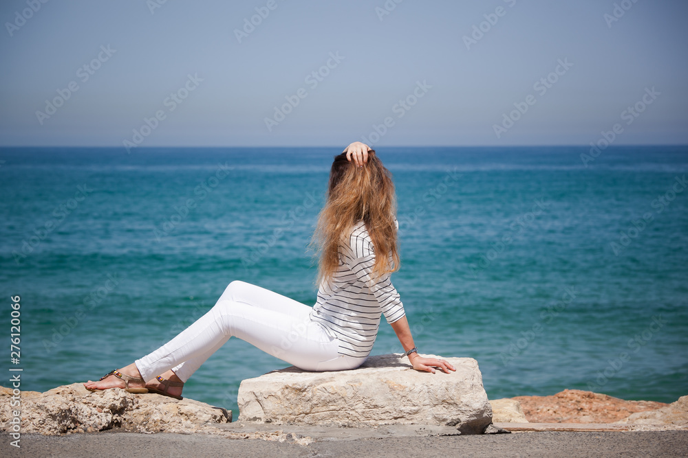 happy european girl sitting on a stone by the sea