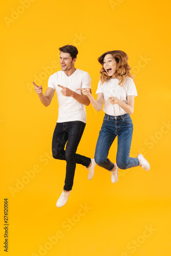 Full length portrait of happy couple man and woman in basic t-shirts smiling while pointing fingers aside at copyspace