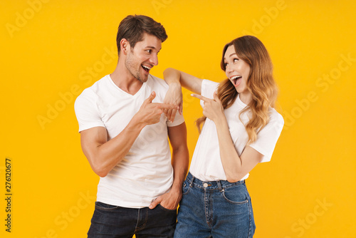 Portrait of content couple man and woman in basic t-shirts rejoicing and pointing fingers at each other