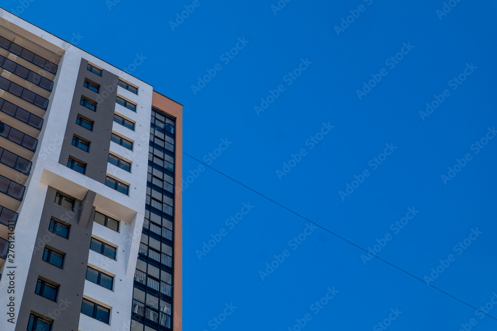 New high-rise building on the background of a clear blue sky. Place for text. Modern new building with balconies and multi-colored facade New high-rise building on the background of a clear blue sky. Place for text. Modern new building with balconies and multi-colored facade