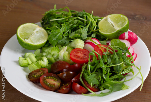 Fresh vegetables as tomato, radish, sliced celery, rosemary and lime on white plate