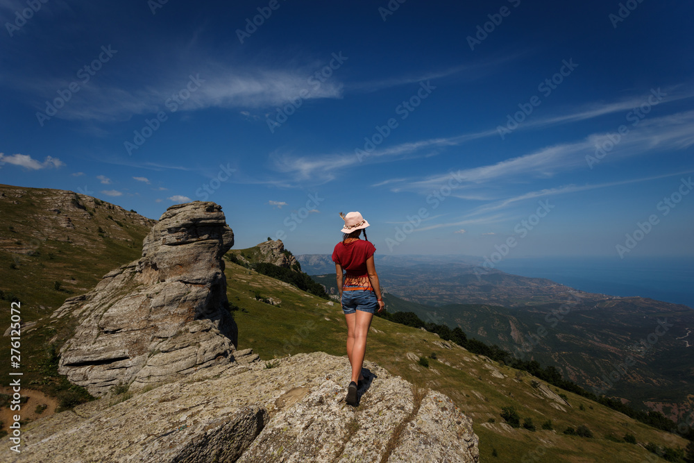 The concept of overcoming, rest and freedom. A woman with tanned legs is standing on top with her arms wide open on either side. Near the rocks of unusual shape. 