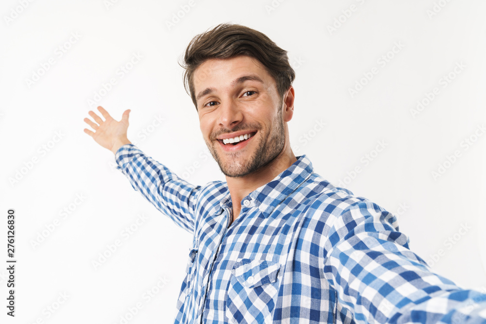 Smiling handsome young man standing isolated over white wall background dressed in casual shirt make selfie by camera showing copyspace. Smiling handsome young man standing isolated over white wall background dressed in casual shirt make selfie by camera showing copyspace.