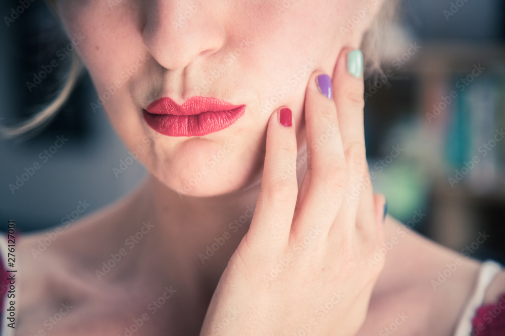Fototapeta premium Attractive red lip stick: Blonde young woman with colorful nail polish is looking herself in the mirror. Cut out of the face.