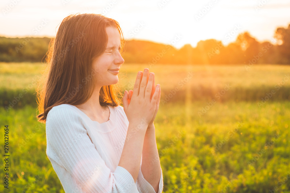 Teenager Girl closed her eyes, praying in a field during beautiful sunset. Hands folded in prayer concept for faith, spirituality and religion. Peace, hope, dreams concept Teenager Girl closed her eyes, praying in a field during beautiful sunset. Hands folded in prayer concept for faith, spirituality and religion. Peace, hope, dreams concept