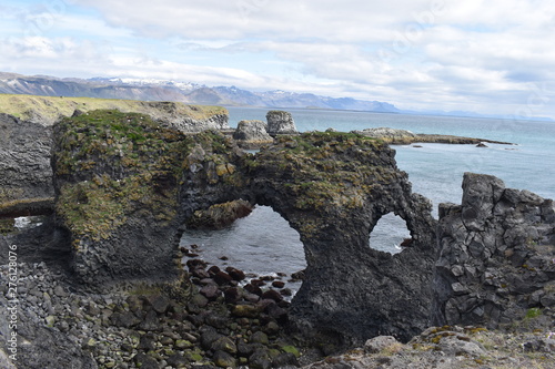 Hiking trail from Anarstapi to Hellnar with the raw ocean und big rocks and mountains and a stone gate in the west of Iceland at Snaefellsnes Peninsula