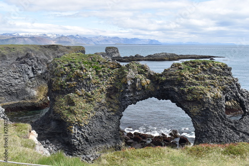 Hiking trail from Anarstapi to Hellnar with the raw ocean und big rocks and mountains and a stone gate in the west of Iceland at Snaefellsnes Peninsula