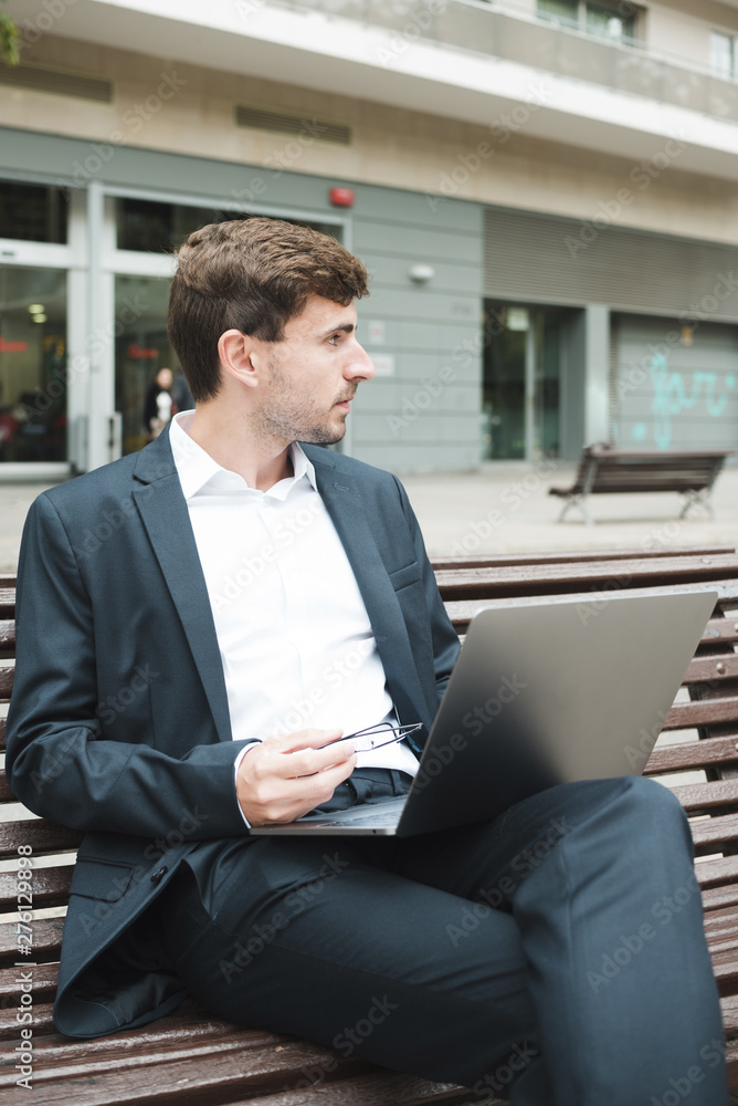 Young businessman sitting on bench with laptop Young businessman sitting on bench with laptop