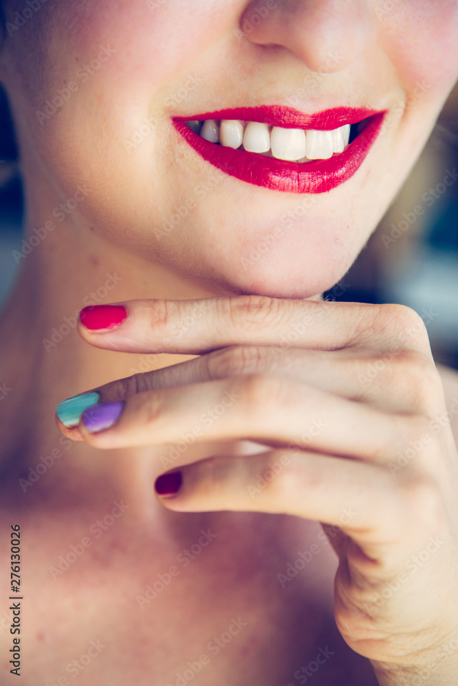 Obraz premium Attractive red lip stick and healthy white teeth: Blonde young woman with colorful nail polish is looking herself in the mirror.