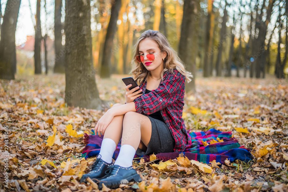Beautiful Autumn Woman with Autumn Leaves on Fall Nature Background. Red lips. Red sunglasses. Sweet young girl with a phone on a walk Beautiful Autumn Woman with Autumn Leaves on Fall Nature Background. Red lips. Red sunglasses. Sweet young girl with a phone on a walk