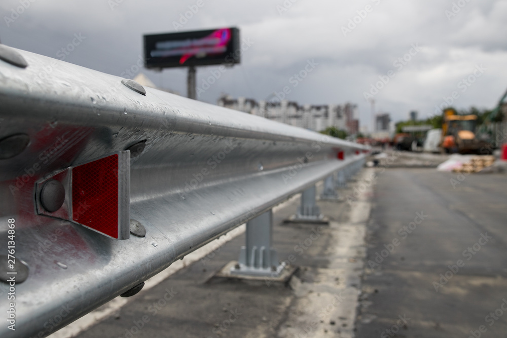 Red road reflectors along the road. Zinked or galvanized metal road fencing of barrier type, close-up. Road and traffic safety. Selective focus with shallow depth of field. Red road reflectors along the road. Zinked or galvanized metal road fencing of barrier type, close-up. Road and traffic safety. Selective focus with shallow depth of field.