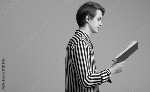 Young handsome man in striped shirt reading a book on gray background