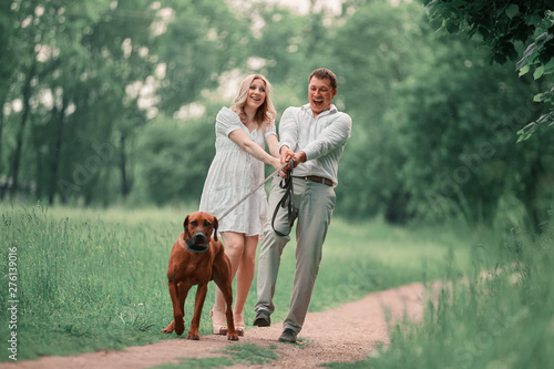 young husband and his wife with their pet dog on a walk in the Park