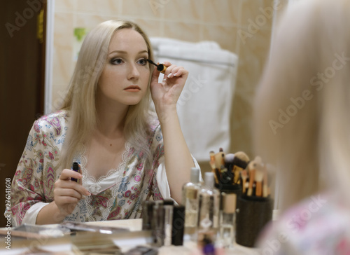 Young woman looking in mirror while applying makeup. Selective soft focus.
