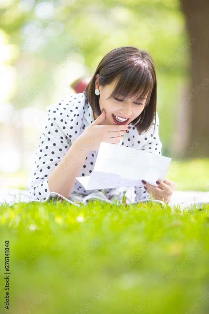 Beautiful young woman reading letter on blanket outdoors