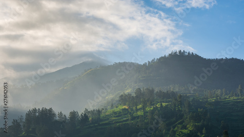 looking up at a mountain peak with clouds and mist creating a dramatic effect in the afternoon sunlight.