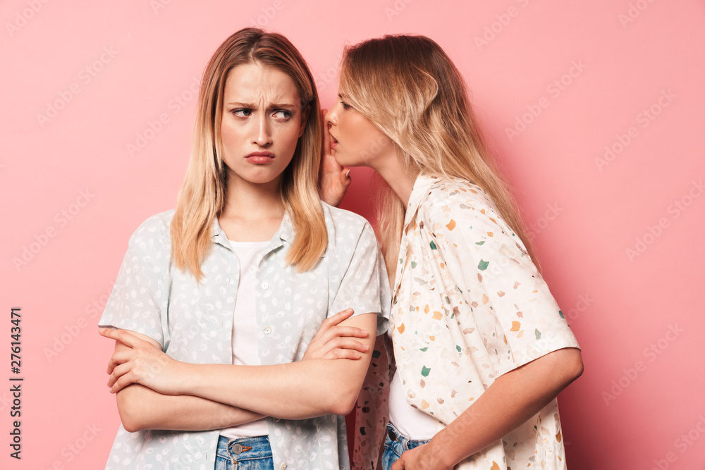 Negative beautiful blondes women friends posing isolated over pink wall background talking with each other gossiping. Negative beautiful blondes women friends posing isolated over pink wall background talking with each other gossiping.