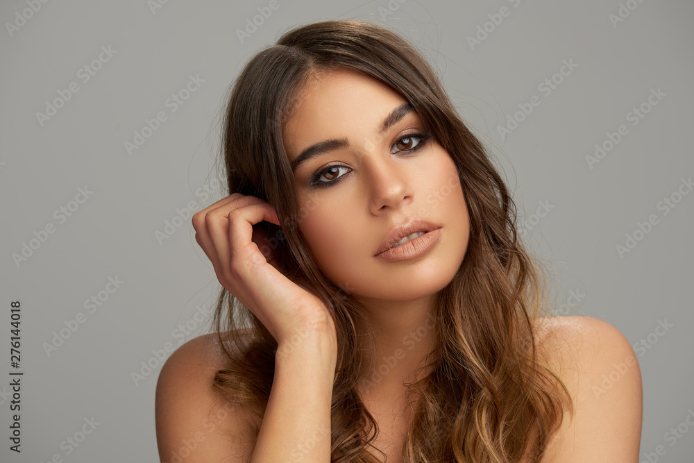 Headshot of beautiful Caucasian brunette posing in front of grey background. Beauty photography. Headshot of beautiful Caucasian brunette posing in front of grey background. Beauty photography.