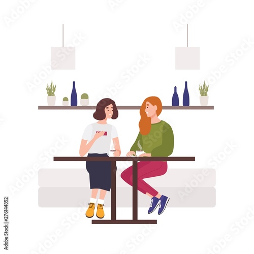 Cute young girls sitting on sofa at cafe, drinking coffee and talking. Two hp...