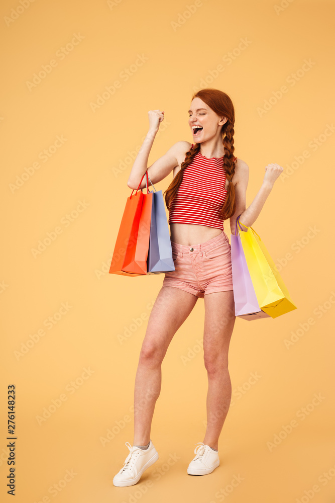 Emotional young beautiful redhead woman posing isolated over yellow background holding shopping bags. Emotional young beautiful redhead woman posing isolated over yellow background holding shopping bags.