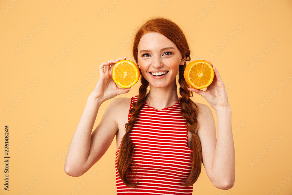 Cheerful  young beautiful redhead woman posing isolated over yellow background holding orange.