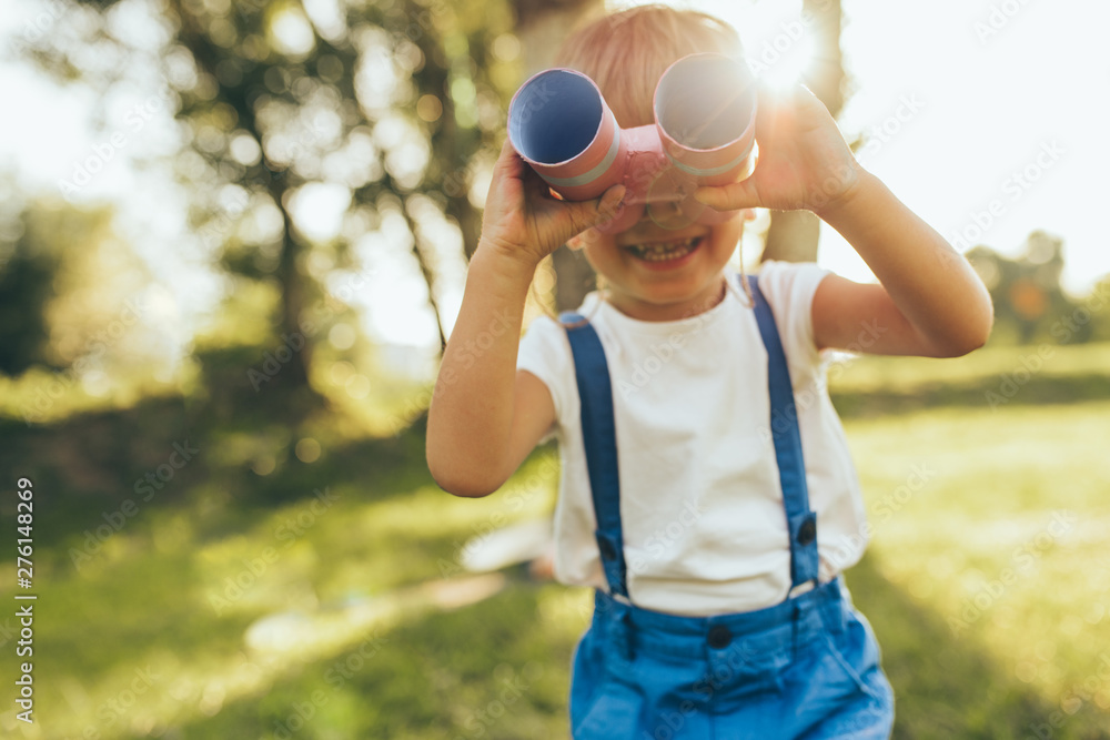 Outdoors closeup portrait of little boy playing with a binoculars searching for an imagination or exploration in summer day in park. Happy child playing pretend safari game outdoors in the forest. Outdoors closeup portrait of little boy playing with a binoculars searching for an imagination or exploration in summer day in park. Happy child playing pretend safari game outdoors in the forest.