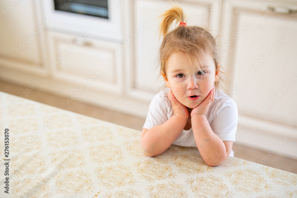 Fototapeta premium Beautiful blonde baby girl having breakfast in kitchen. Funny faces