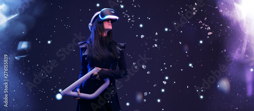 Beautiful woman in futuristic dress over dark background. Gamer girl in glasses of virtual reality with controller in hands. Augmented reality, game, hobby concept. VR.
