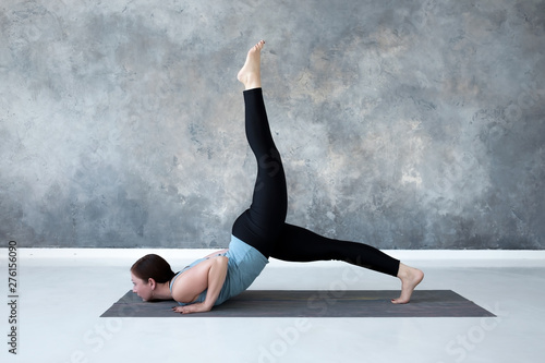 Woman practicing yoga doing eka pada Shalabhasana, the Locust pose variation in full length photo