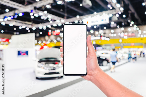 Mock up mobile phone. Hand holding mobile phone with abstract blurred cars exhibition show background image. Car shopping online, internet and social network background concept.