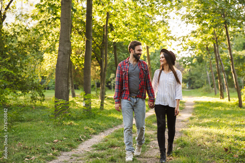 Smiling positive young loving couple walking outdoors in a green nature park forest.
