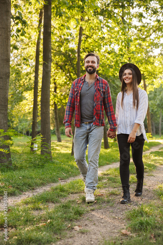 Smiling positive young loving couple walking outdoors in a green nature park forest.