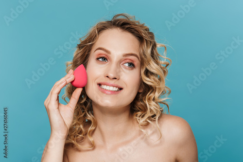 Image of pleased half-naked woman applying makeup with sponge