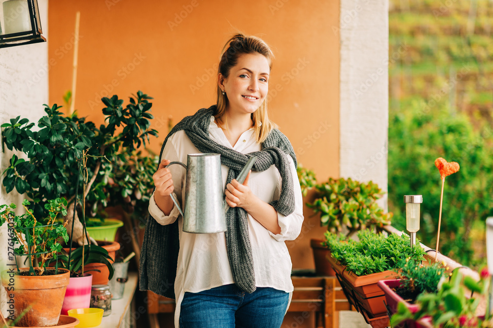 Portrait of beautiful woman watering green plants on the balcony, small cozy garden in apartment Portrait of beautiful woman watering green plants on the balcony, small cozy garden in apartment